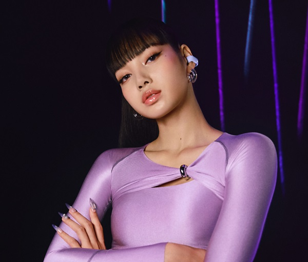 Kobieta w fioletowym stroju z długimi paznokciami i kolczykami, pozująca do zdjęcia, ciemne tło.