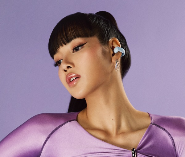 Kobieta z niebieską słuchawką i makijażem na fioletowym tle.