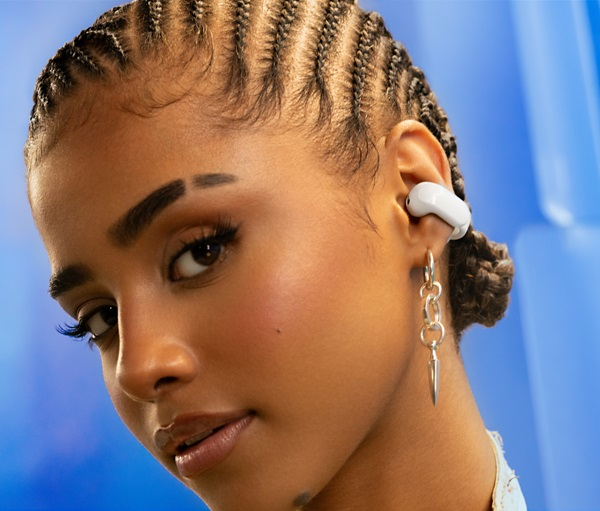 Młoda kobieta z warkoczami nosi białą słuchawkę i kolczyki, niebieskie tło.