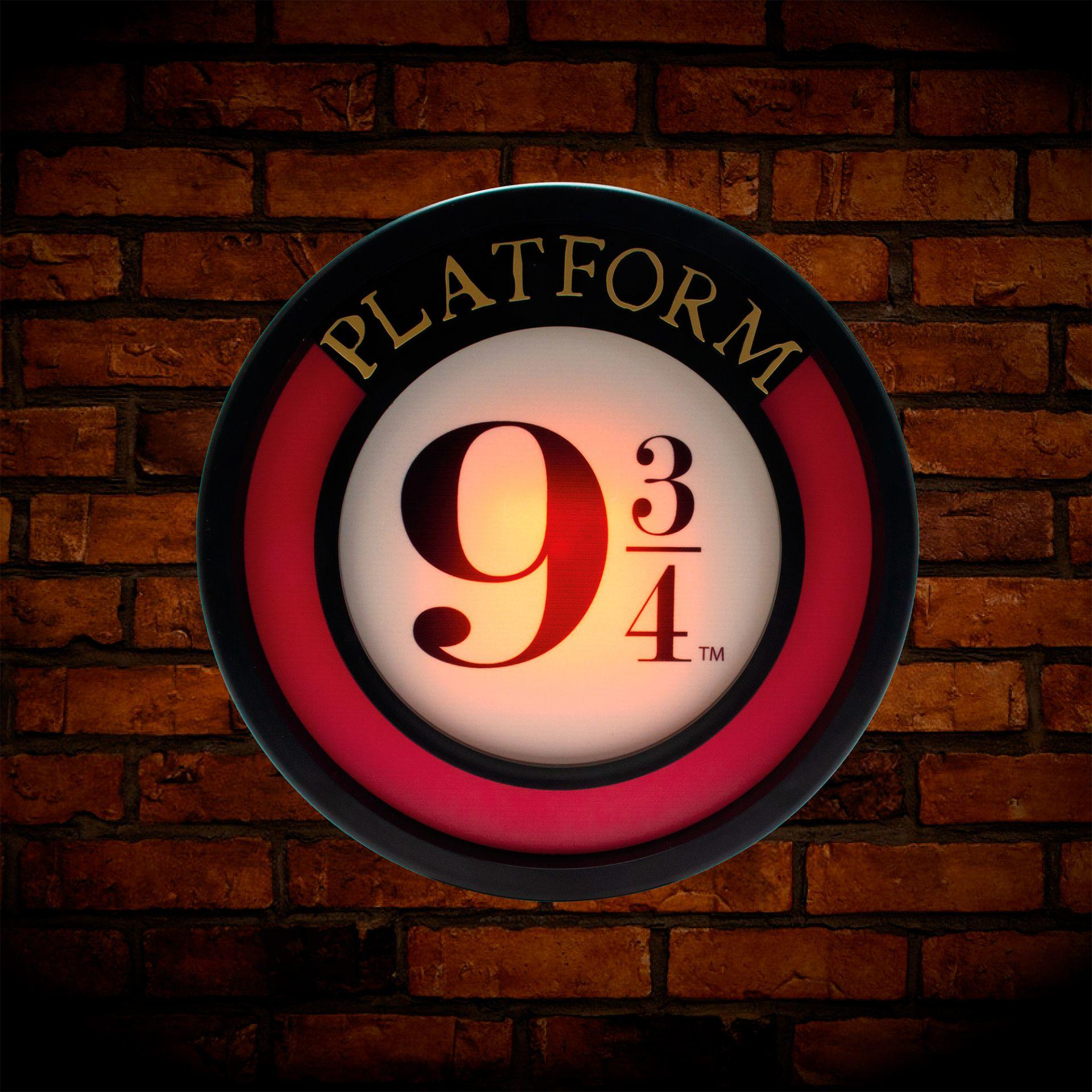 Ein beleuchtetes Platform 9 3/4 Schild, kreisförmig, mit roten und schwarzen Akzenten, Ziegelhintergrund.