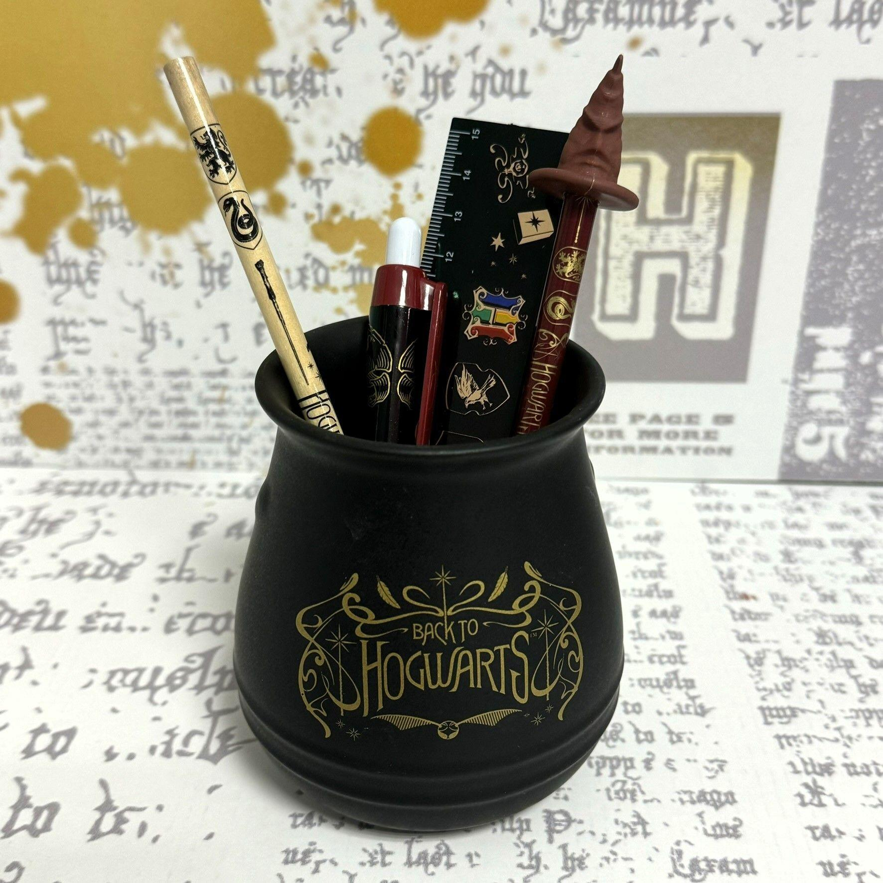 Ein schwarzer Kessel mit "BACK TO HOGWARTS" und Harry Potter-Schreibwaren darin, auf einer gemusterten Oberfläche.