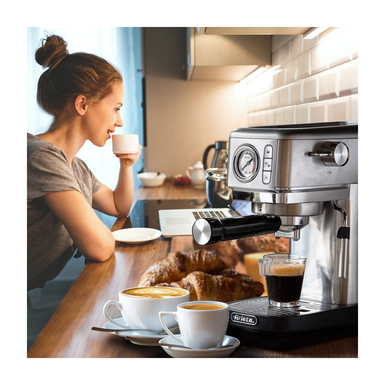 Donna che beve caffè, macchina per l'espresso, croissant e laptop in cucina.