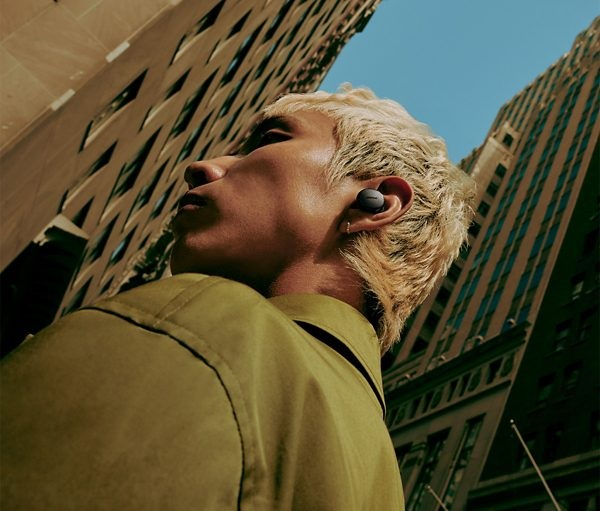 Osoba w słuchawkach na ulicy miasta, patrząca na budynki.