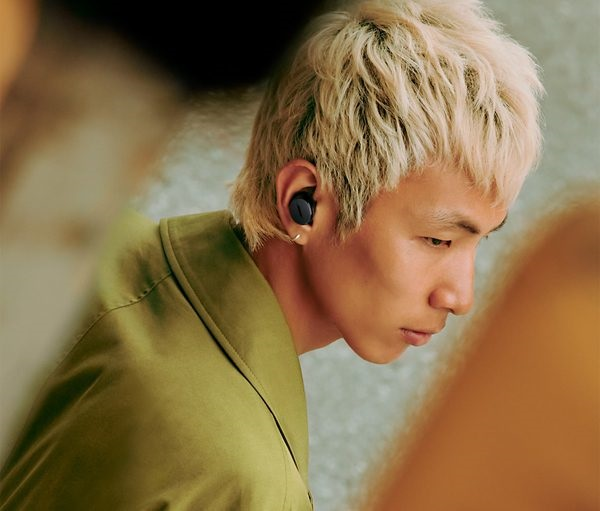 Mężczyzna z blond włosami noszący słuchawki. Ma na sobie zieloną koszulę i patrzy w dół.