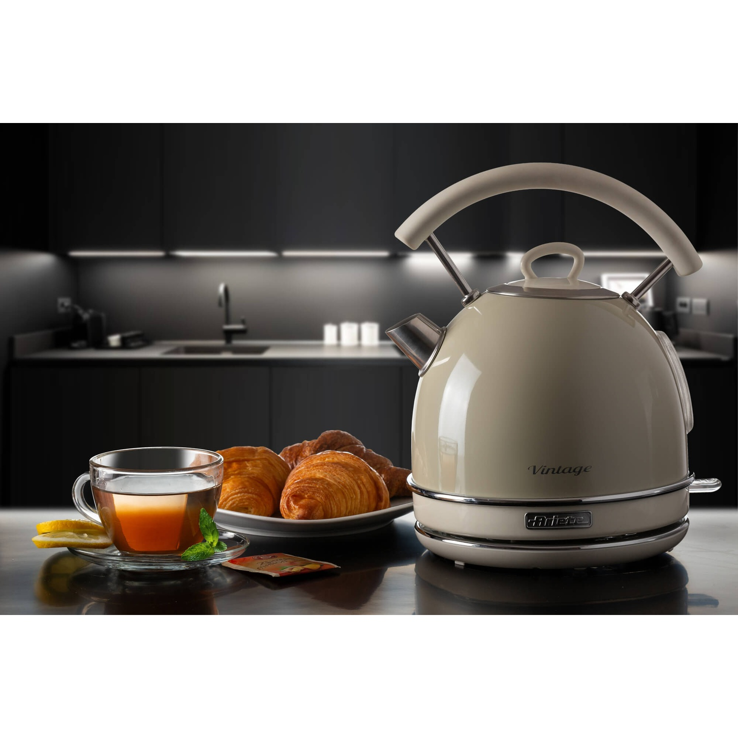 Bollitore in stile vintage con tè e croissant. Bollitore beige, tazza da tè, piatto di croissant su superficie nera.