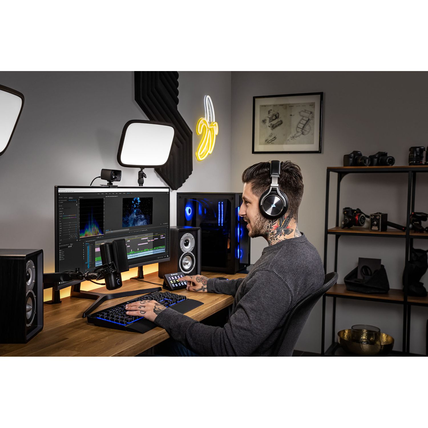 A man with headphones is sitting at a desk with a computer, microphone, and equipment.