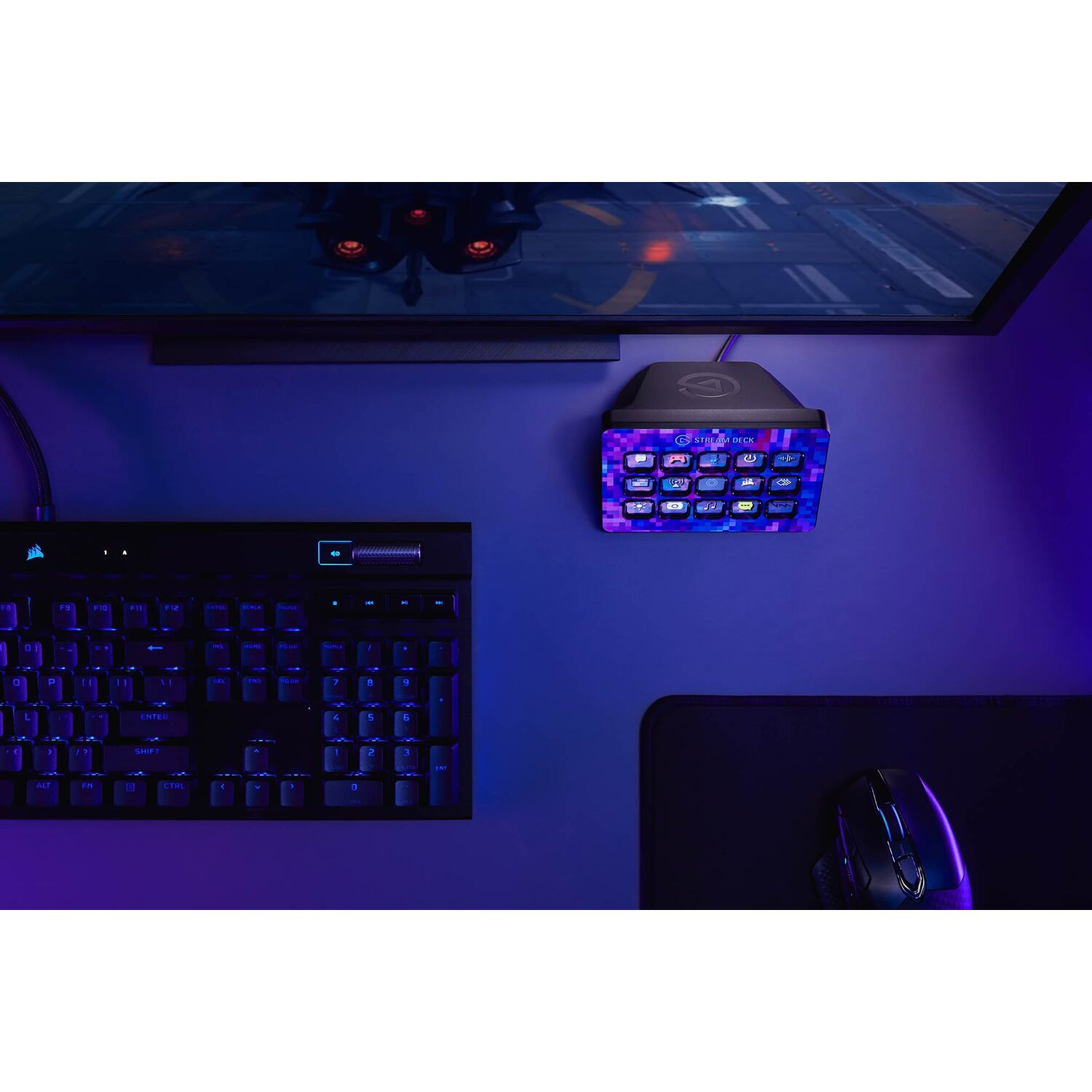 A gaming desk setup with a keyboard, mouse, and a Stream Deck controller mounted on the wall.