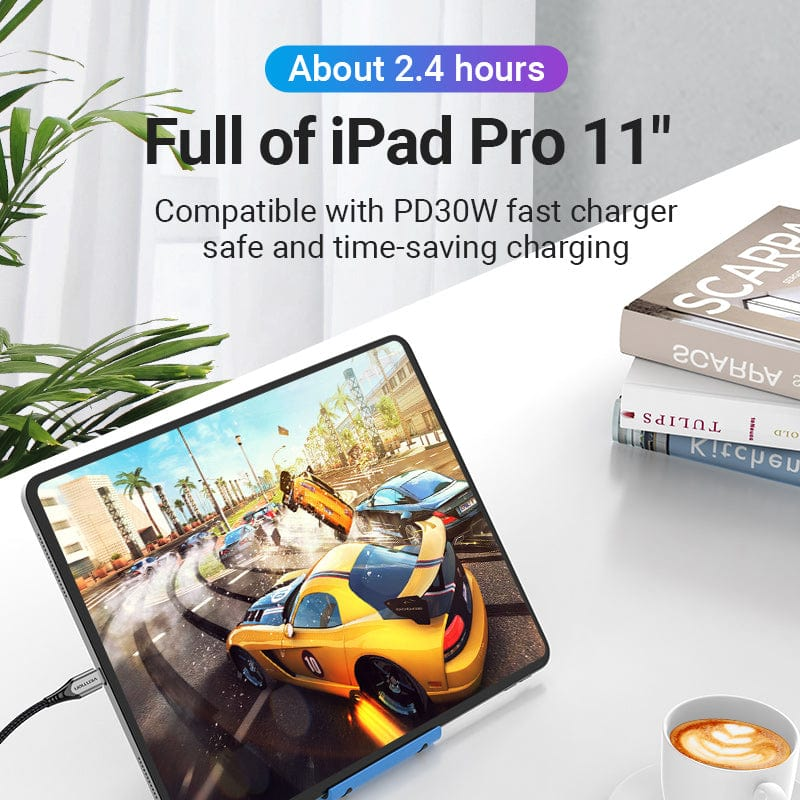iPad Pro autóverseny játékkal, töltés közben. Könyvek és kávé az asztalon. Zöld növény.