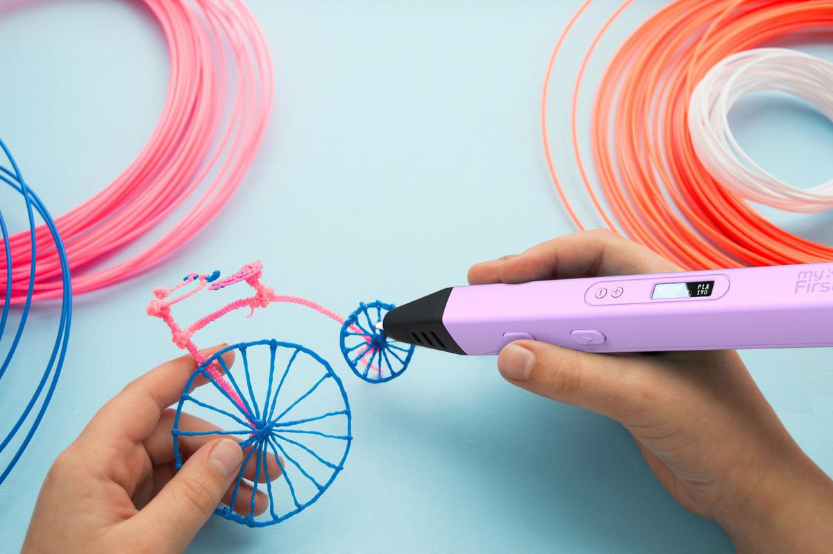 Eine Person erstellt mit einem 3D-Stift ein 3D-Modell eines Fahrrads. Es gibt bunte Filamente.
