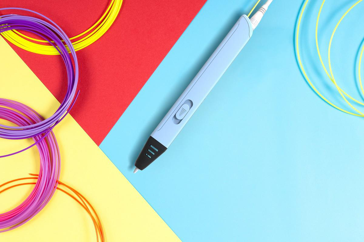 3D-Stift mit bunten Filamenten auf einem dreifarbigen Hintergrund: rot, gelb und blau.