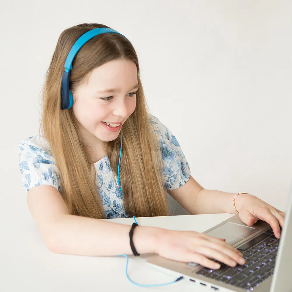 Una ragazza con cuffie blu, sorridente mentre usa un laptop, su una superficie bianca.