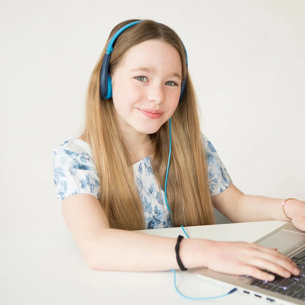 Ragazza con cuffie blu. Sorride e usa un laptop su una superficie bianca.