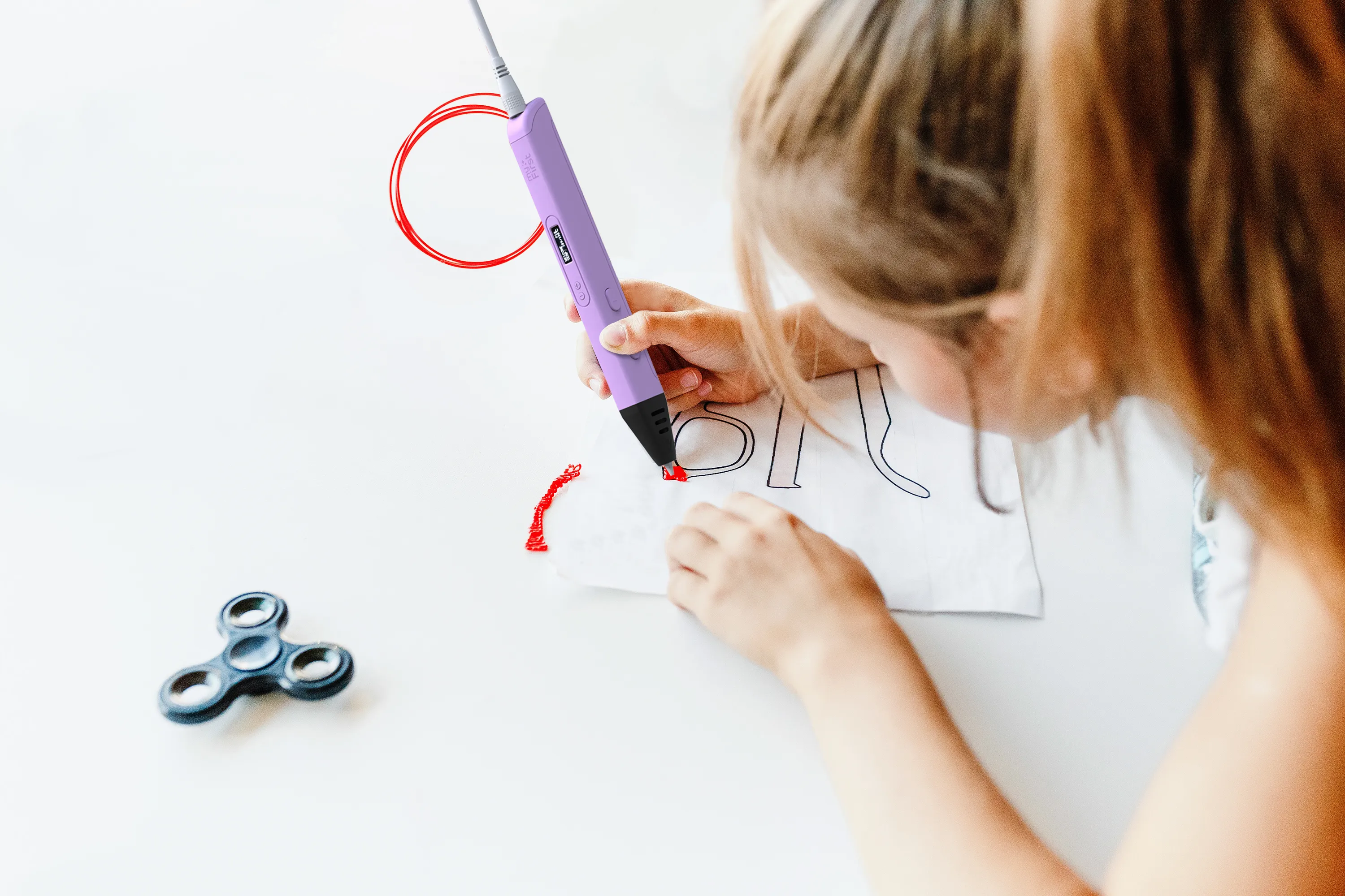 Enfant dessinant avec un stylo 3D violet sur papier blanc, le spinner est visible.