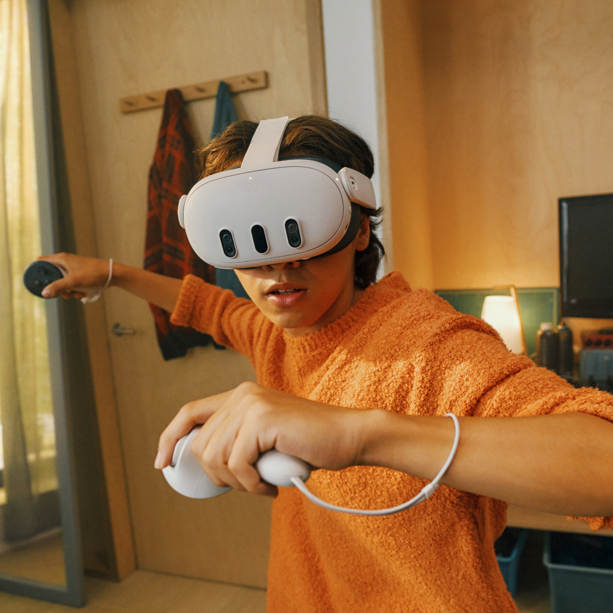 Ein Mann mit VR-Headset und Controllern, in einem orangefarbenen Pullover, in einem Raum.