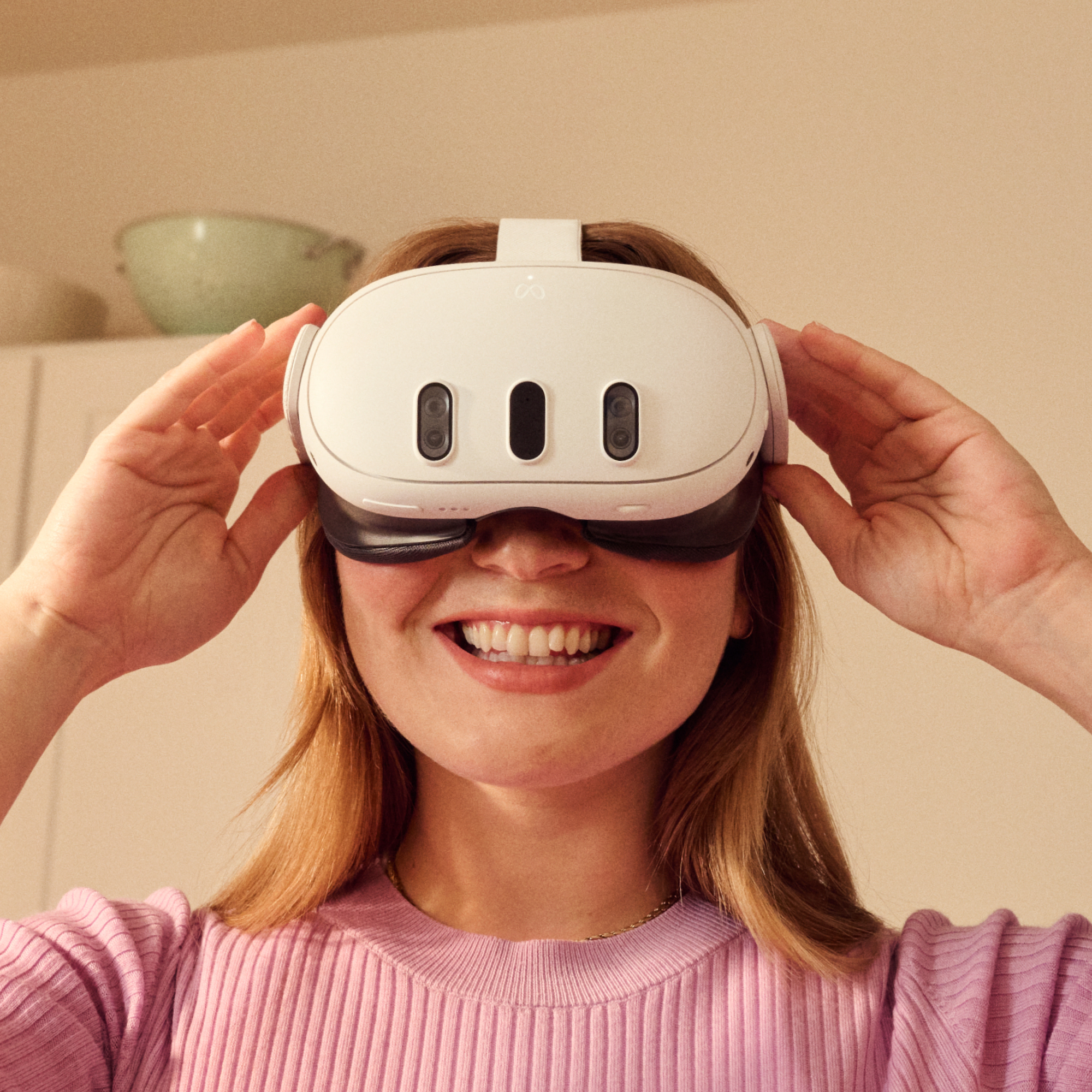 Eine Frau mit einer weißen VR-Brille lächelt. Die Brille hat drei Kameras. Sie trägt ein rosa Oberteil.