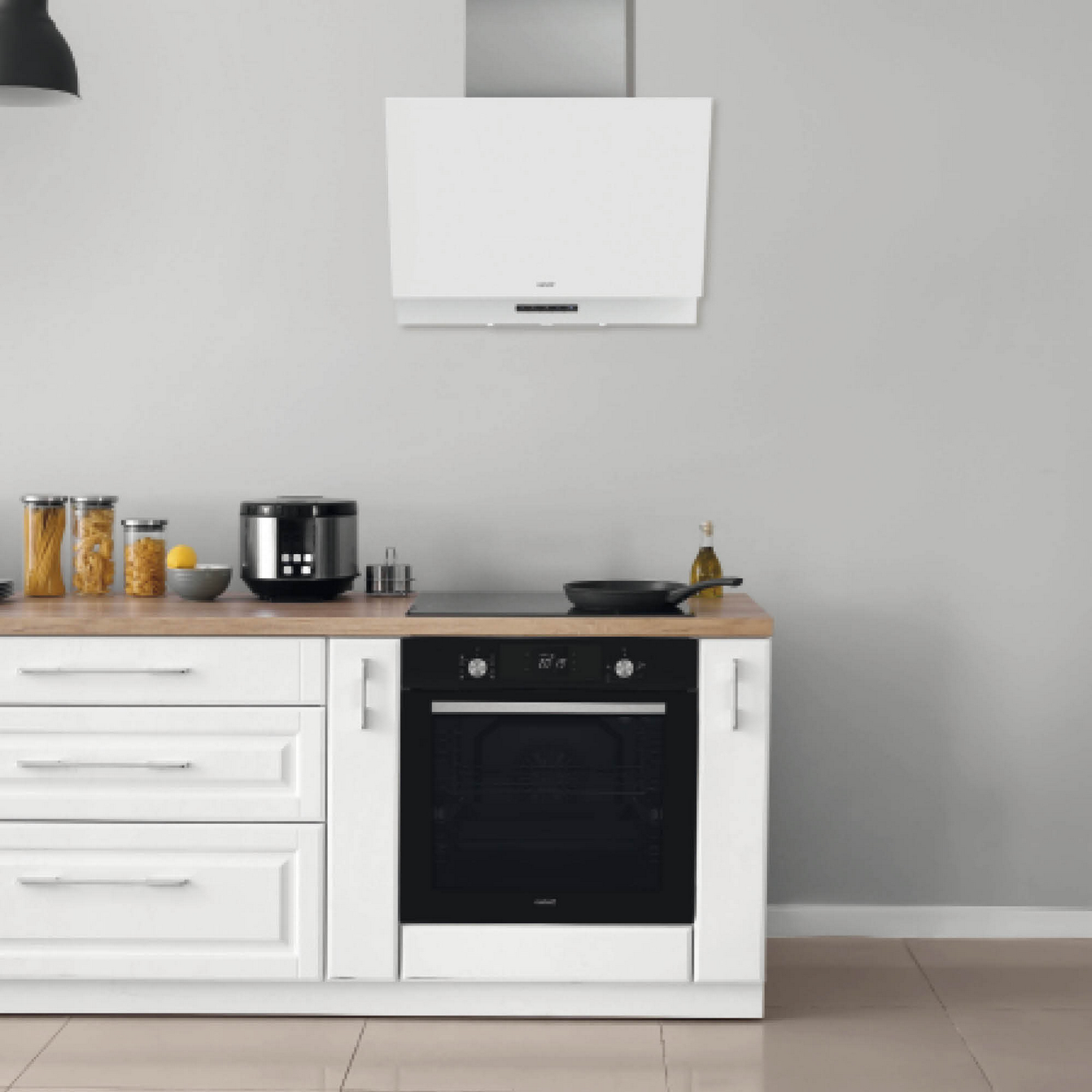 Cocina con armarios blancos, encimera de madera, horno y campana extractora blanca.