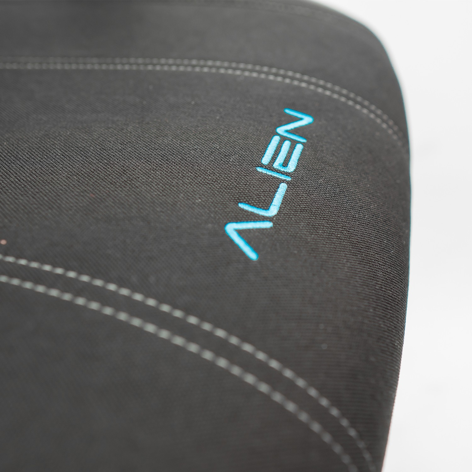 Material negro con costuras blancas y logo ALIEN azul. Primer plano sobre fondo blanco.