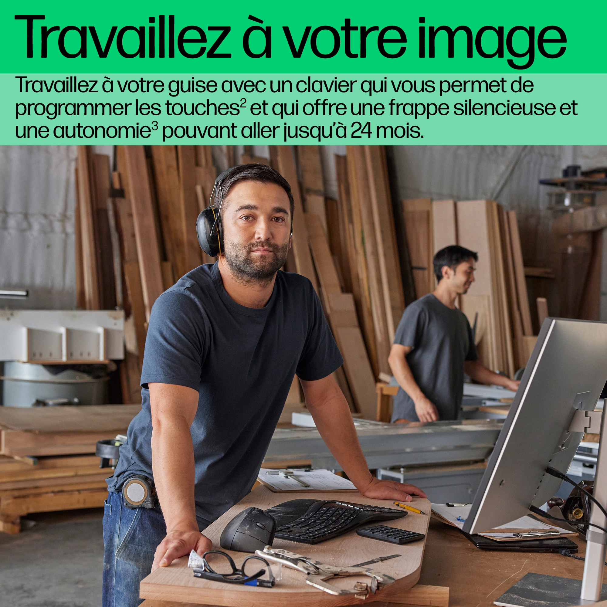 Un homme portant un casque est appuyé sur une table en bois. Un autre homme travaille à droite.
