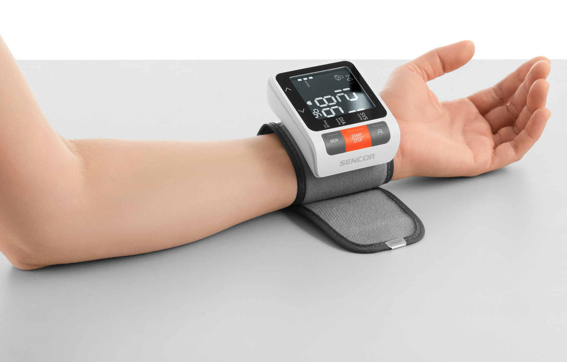 Osoba nosząca monitor ciśnienia krwi na nadgarstku. Szary stół.