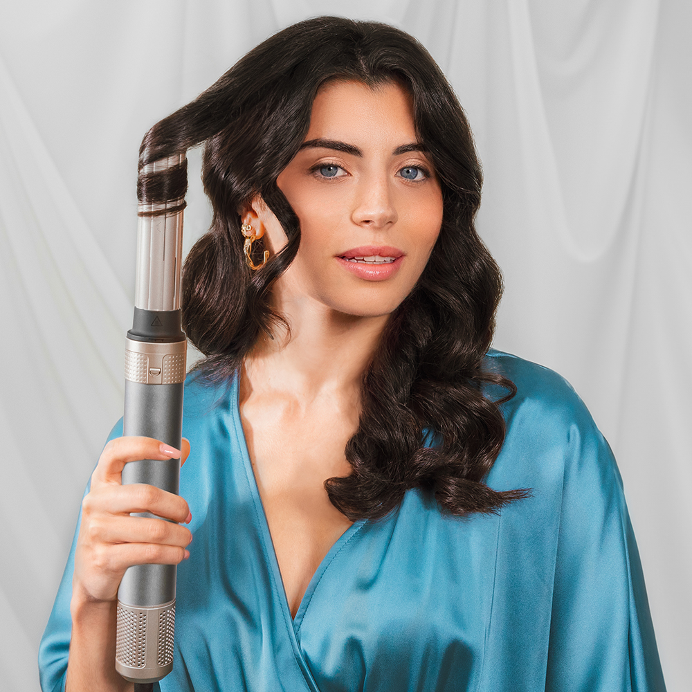 Mujer rizando su cabello con una herramienta de peinado. Lleva una bata azul.