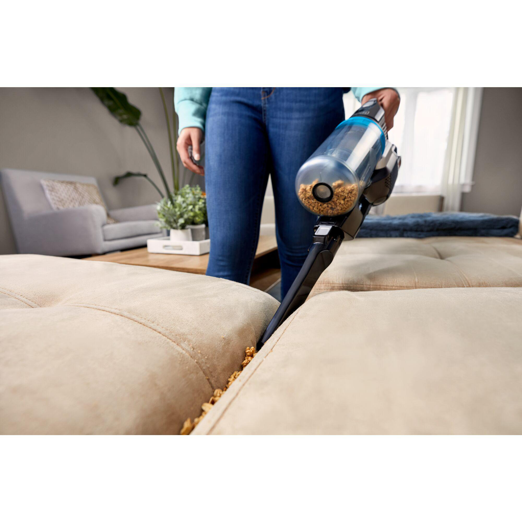 Person saugt Sofa ab, reinigt Ritzen und entfernt Schmutz mit Staubsauger.