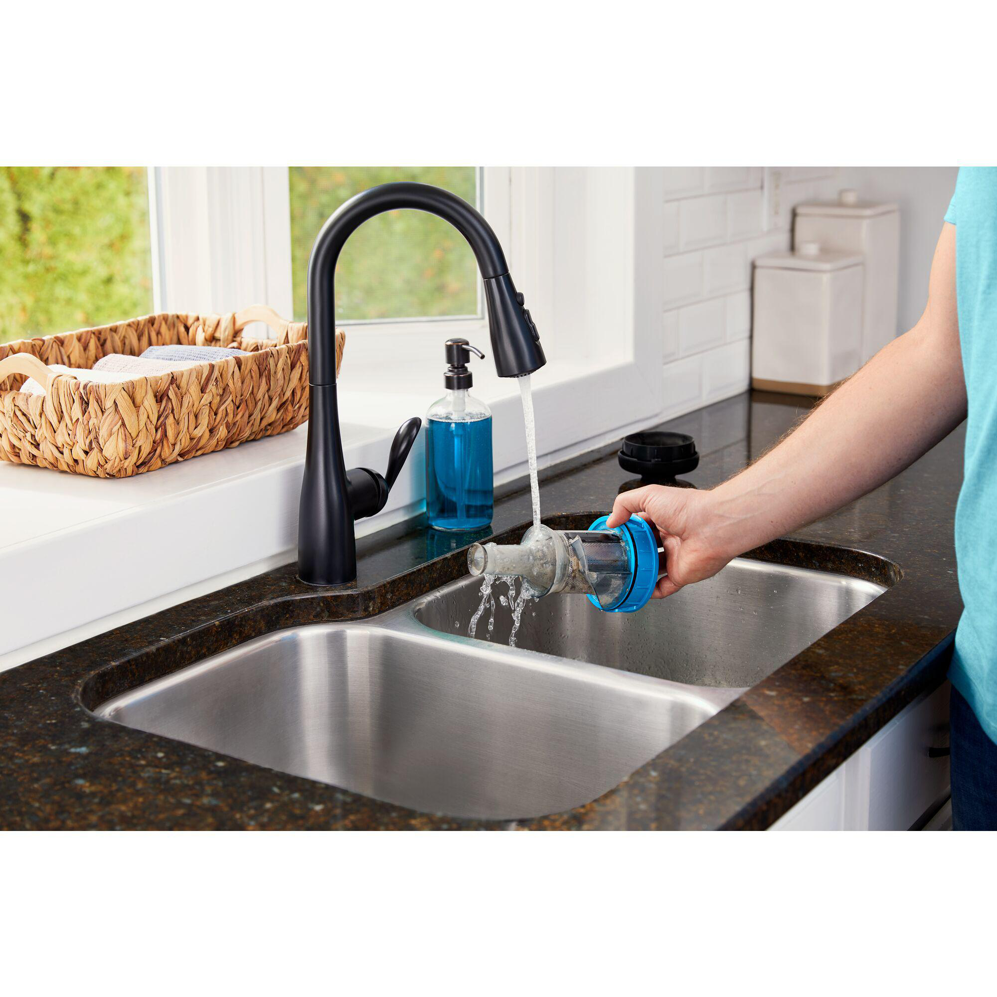 Person wäscht Filter unter Wasserhahn. Der Filter ist blau und wird in der Hand gehalten.