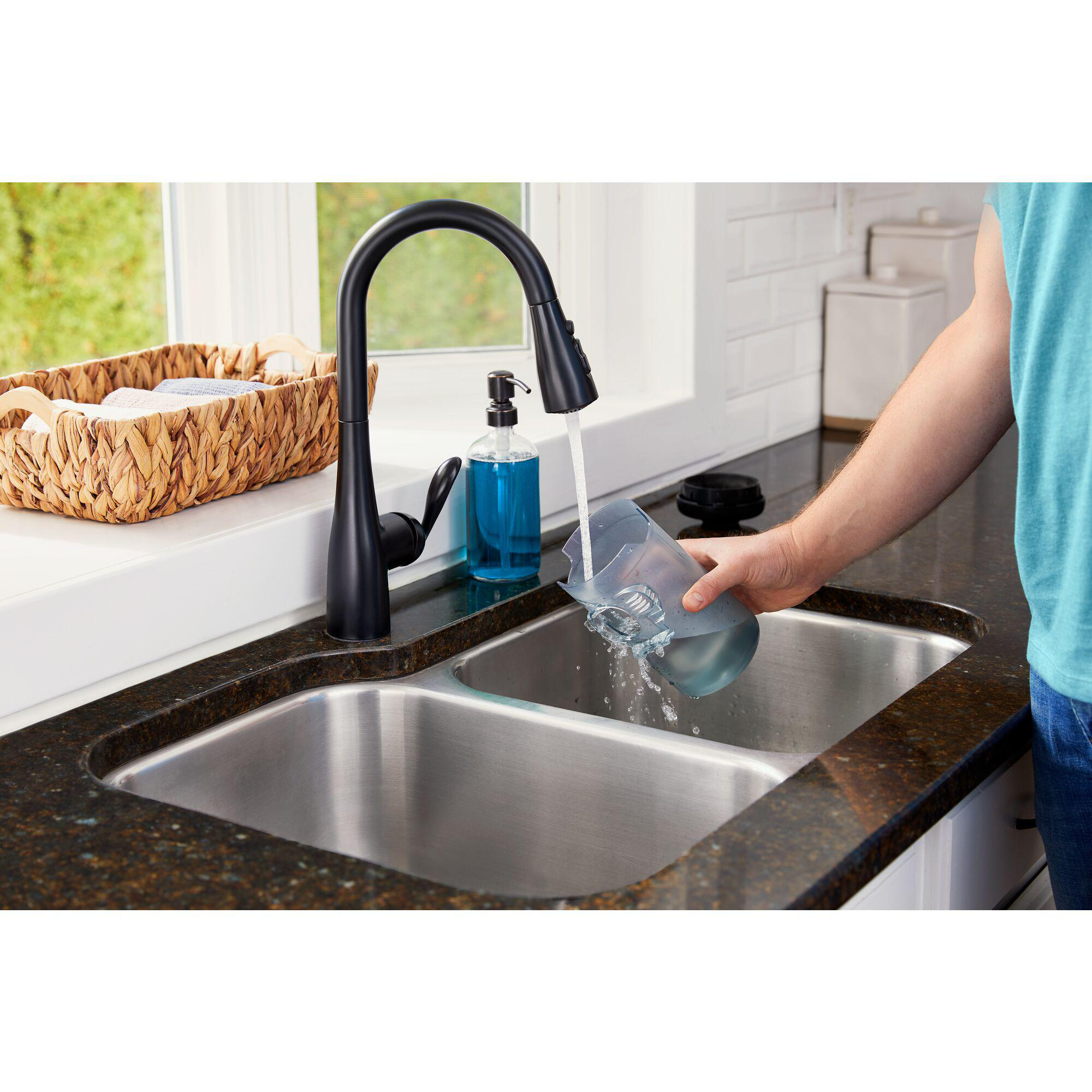 Eine Person gießt Wasser aus einem Messbecher in ein Edelstahlwaschbecken. Küchenumgebung.