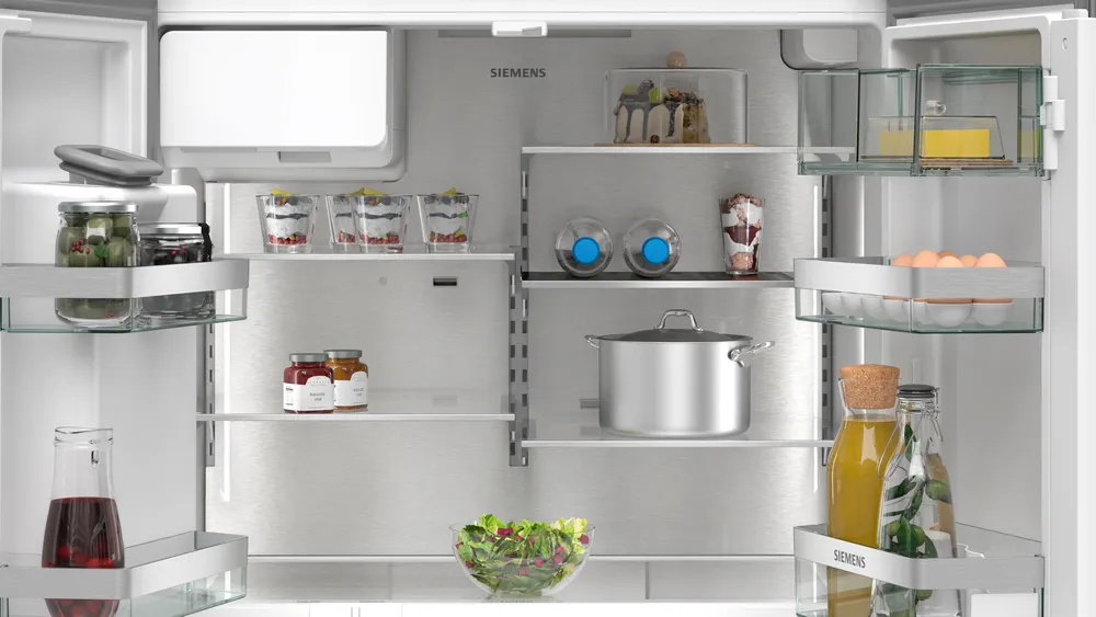 In einem Kühlschrank: Gläser, Desserts, Eier, Salat, Flaschen und ein Topf. Gegenstände befinden sich auf Regalen, meist sichtbar. Der Kühlschrank ist sauber.