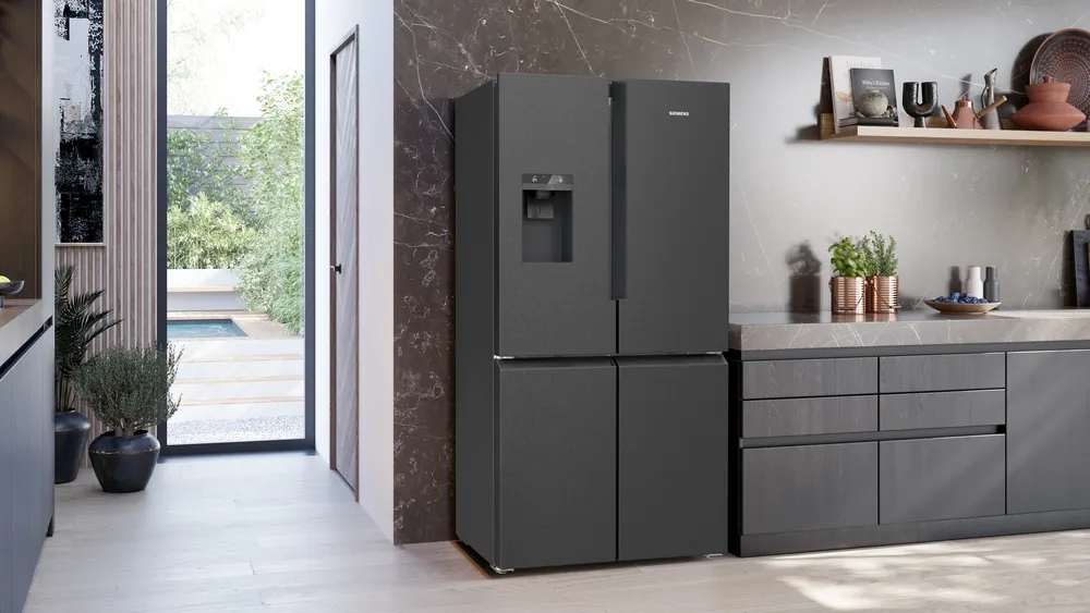 Moderne Küche mit schwarzem Kühlschrank, Blick in einen Garten durch eine Tür und Arbeitsplatte mit Dekoration.