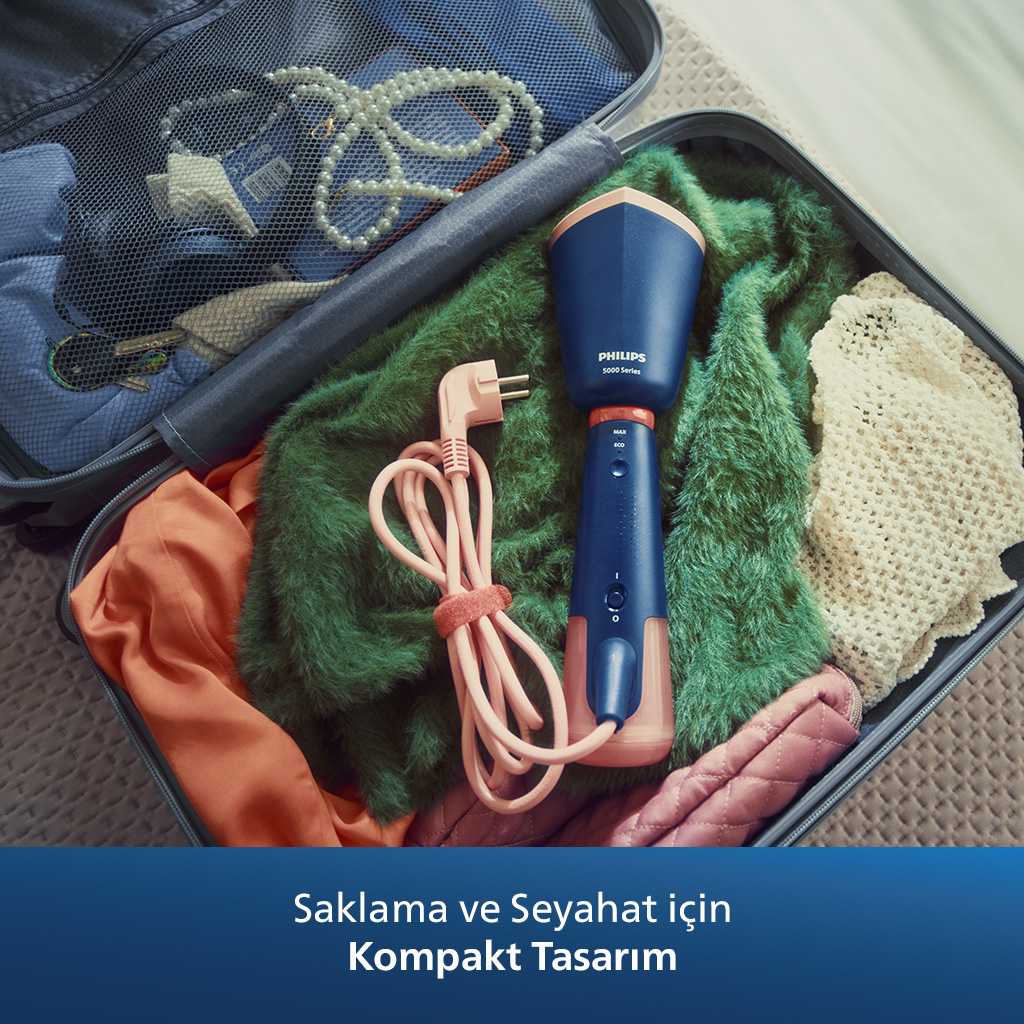 Açık bir bavul içinde giysiler ve aksesuarlarla birlikte bir Philips buhar makinesi ve kablo.
