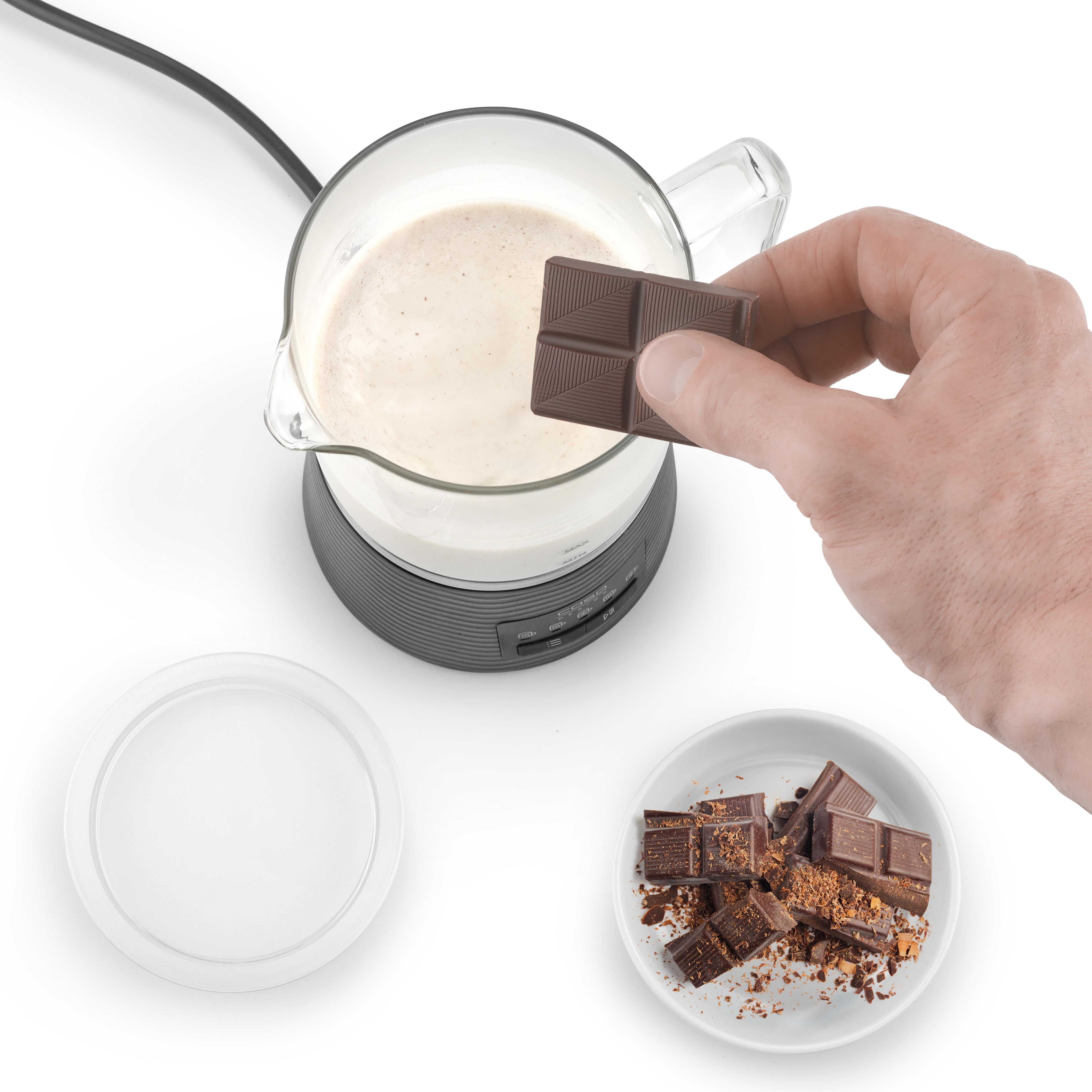 Hand fügt Schokoriegel Milch in einem Glaskrug hinzu, mit Schokostücken in einer Schüssel.