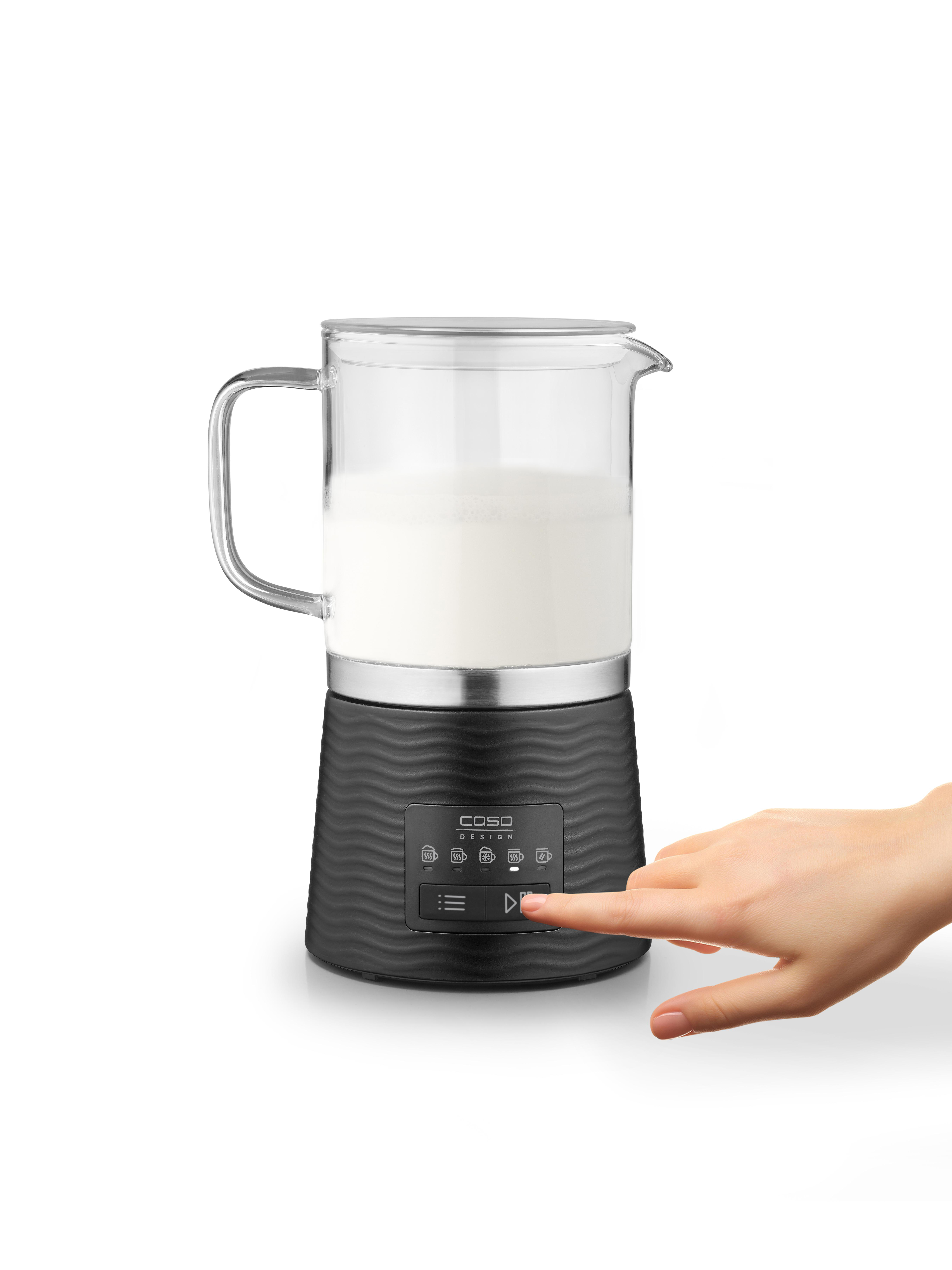 Eine Hand drückt einen Knopf an einem schwarzen Milchaufschäumer mit Milch.