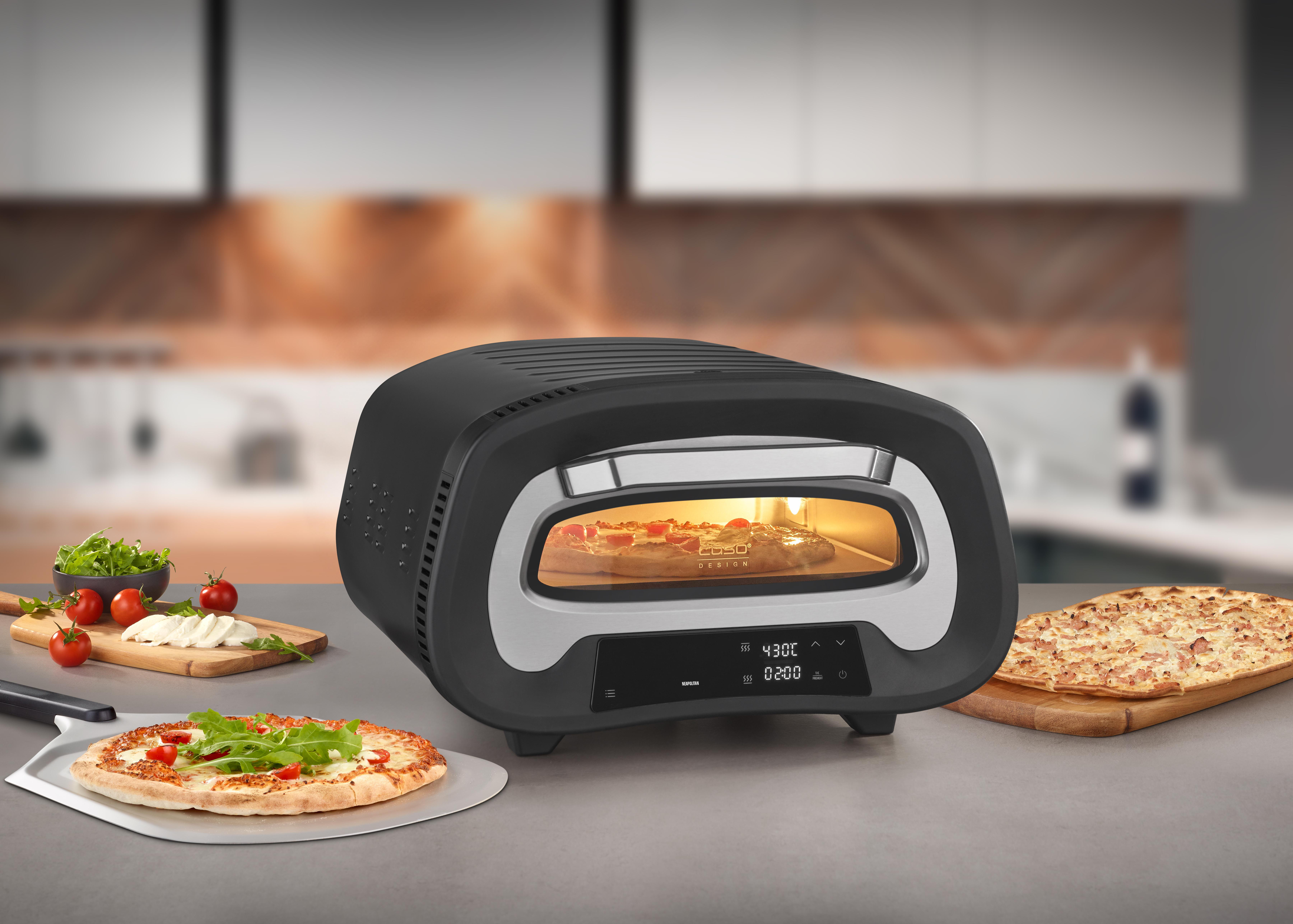 Schwarzer Pizzaofen mit Pizza drin und Pizzen auf einem Brett, mit Zutaten.