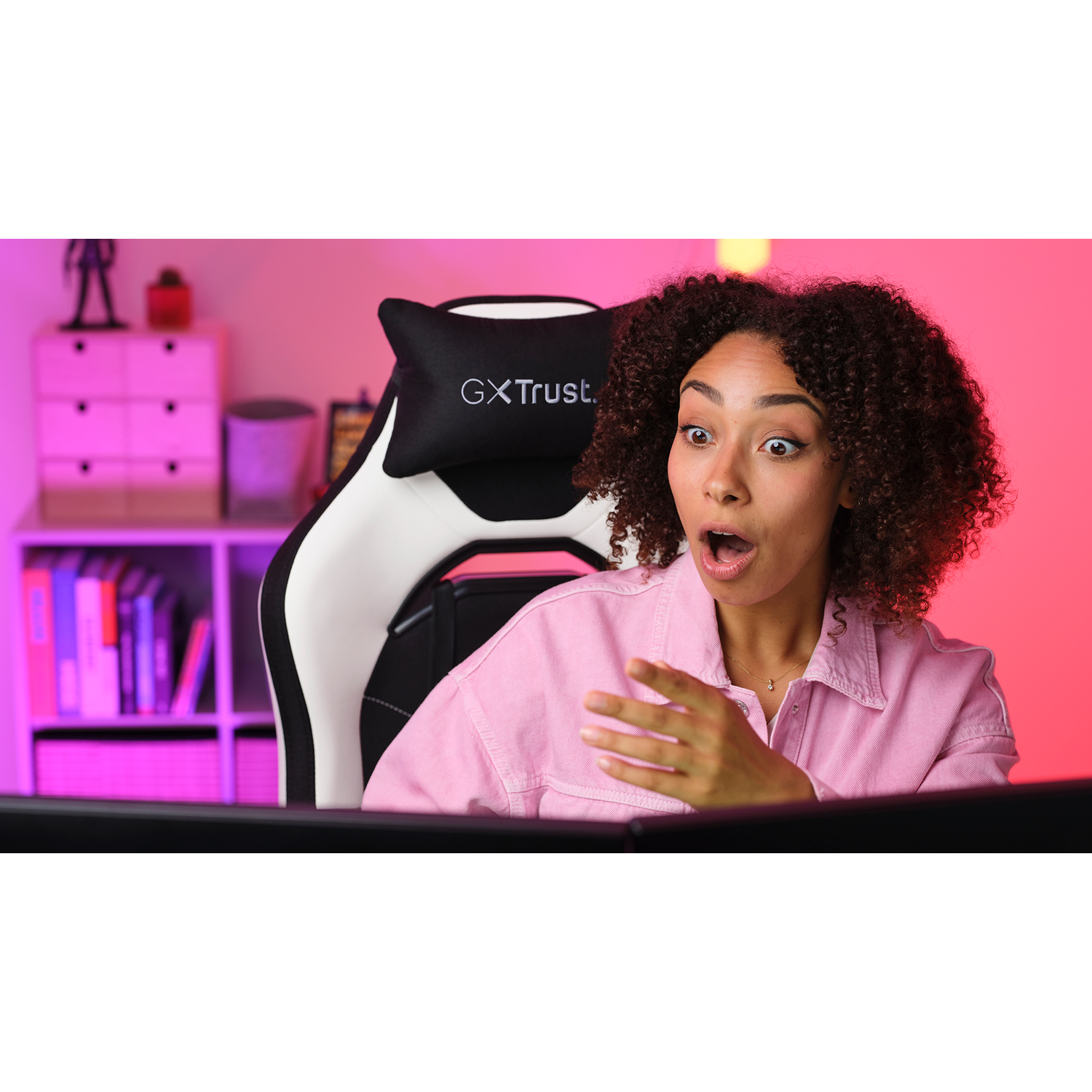 A woman with surprised expression sits in a gaming chair, looking at screen.