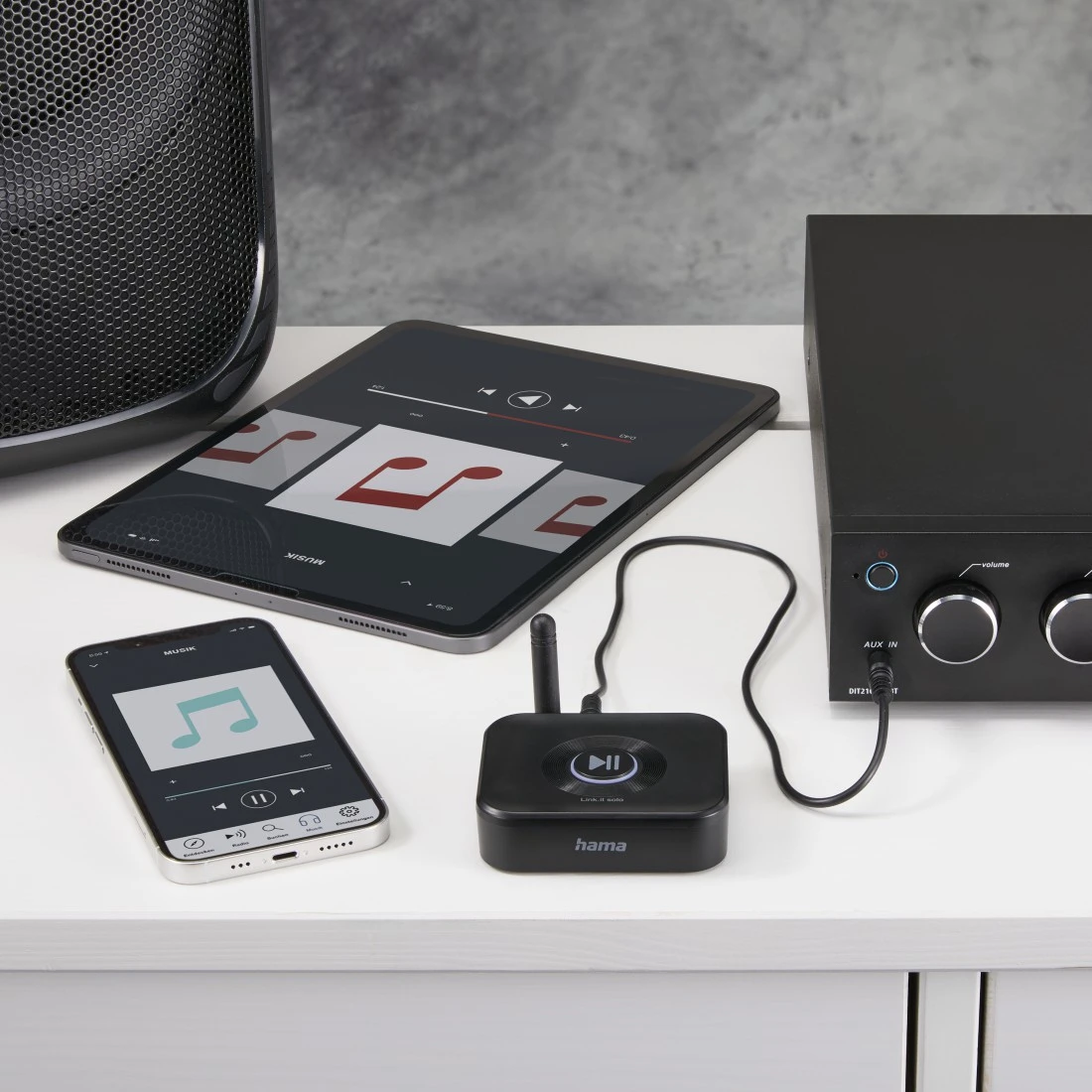Egy tablet és egy telefon zenei alkalmazásokat jelenít meg, egy fekete audioreceiver mellett, csatlakoztatott eszközzel.
