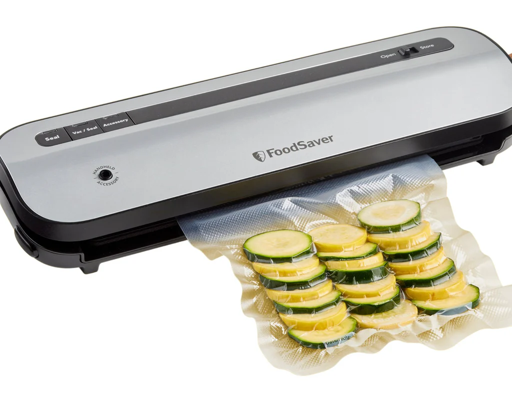 Zgrzewarka próżniowa z plasterkami cukinii w worku do zgrzewania. Zgrzewarka jest szara i czarna.