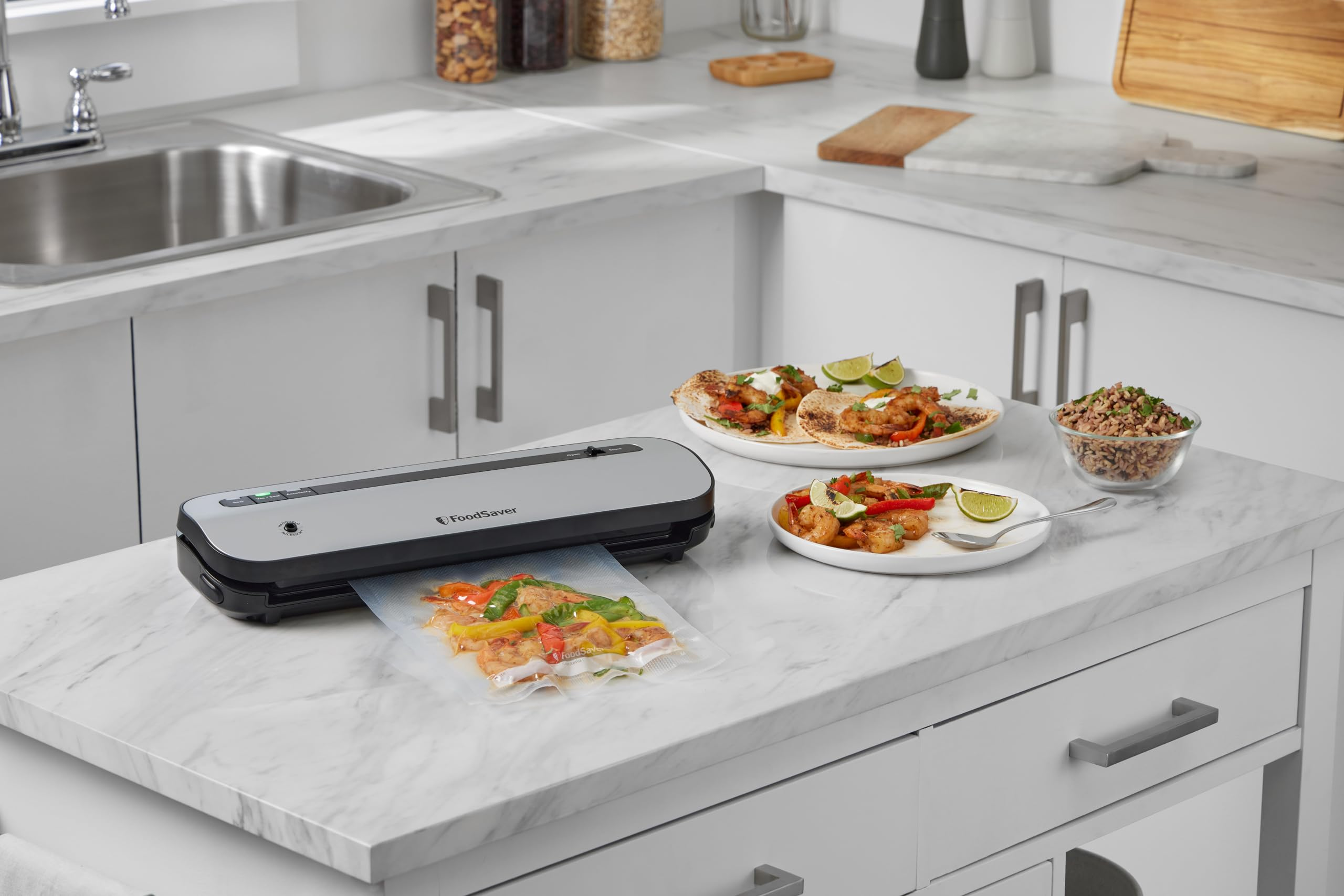 Zgrzewarka próżniowa FoodSaver z torbą wypełnioną jedzeniem i talerzami na blacie.