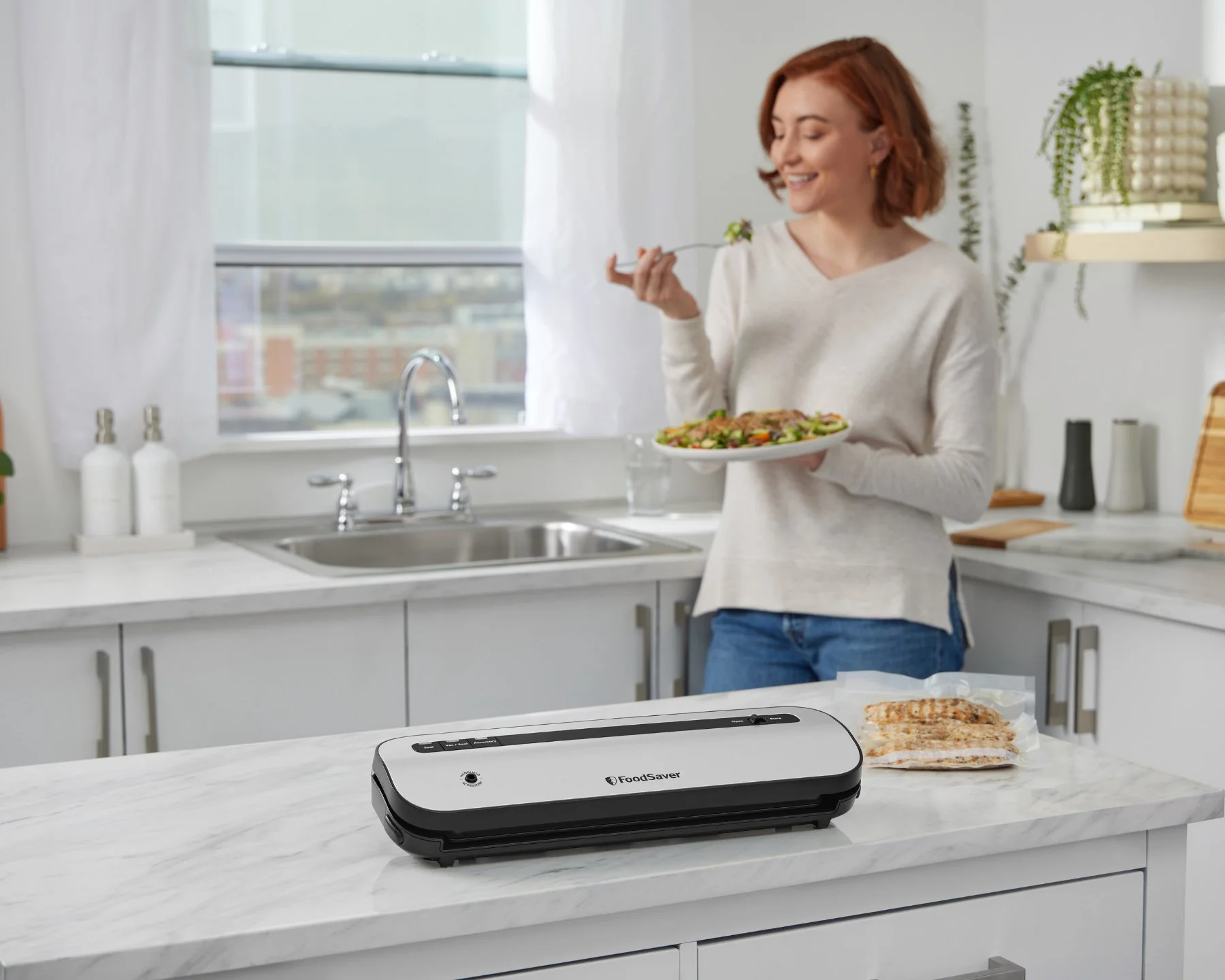 Kobieta w kuchni z jedzeniem. Zgrzewarka próżniowa na blacie, żywność w workach.