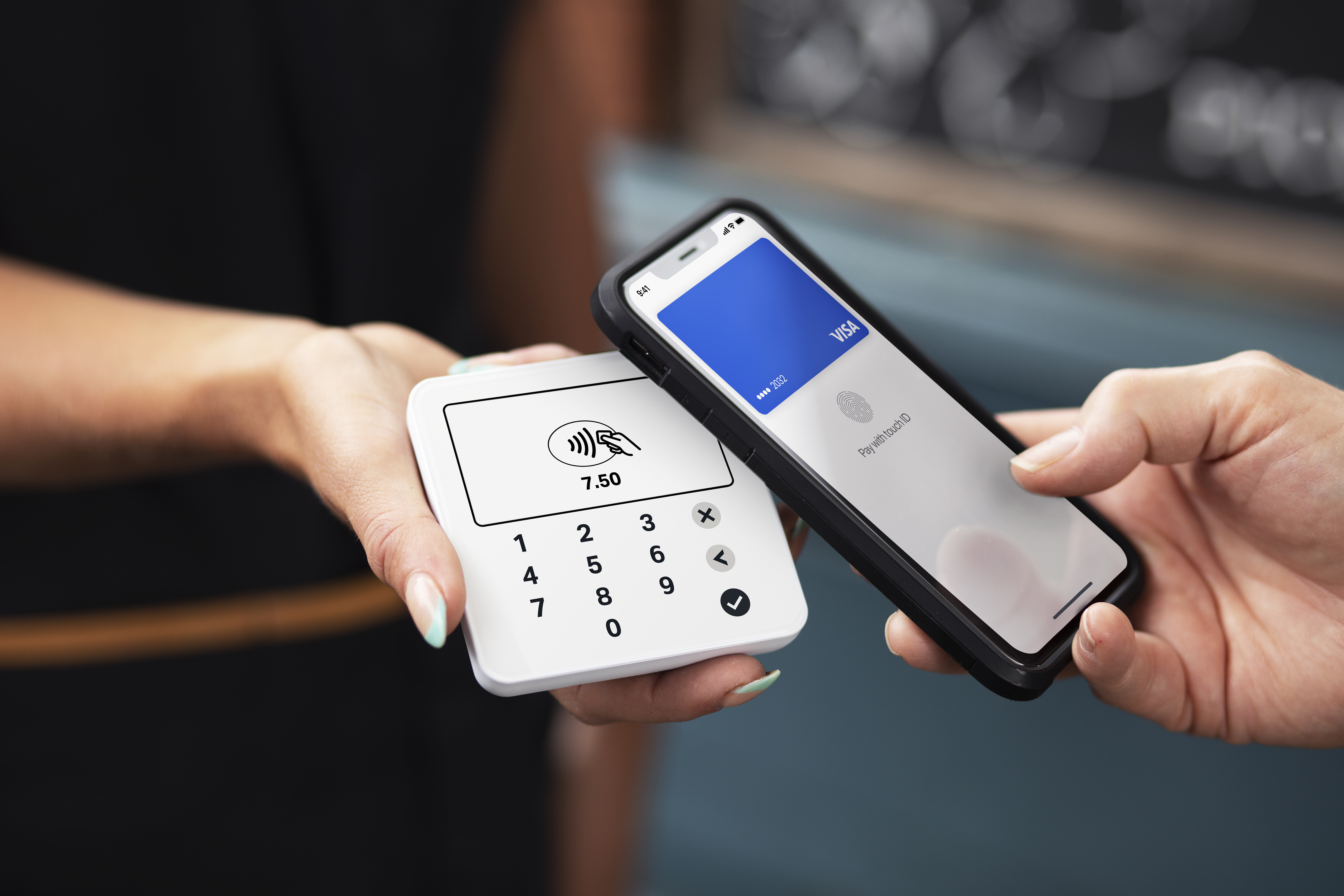 Hände halten ein weißes Zahlungsgerät und ein Telefon. Das Telefon zeigt eine blaue Karte auf dem Bildschirm.