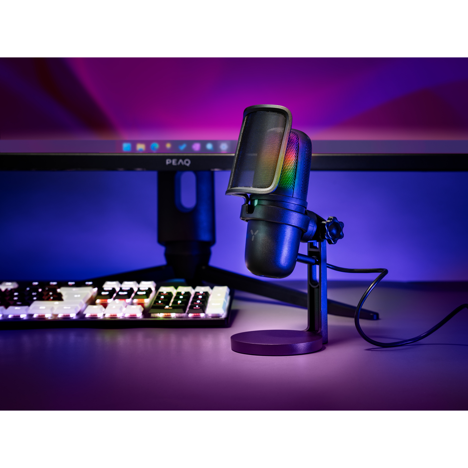 Black microphone on a stand. A keyboard and monitor are in the background. RGB lighting.