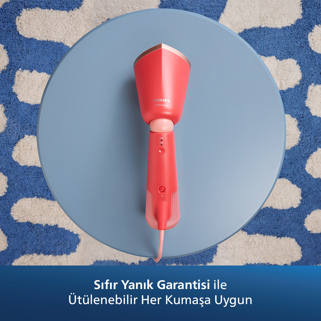 Mavi yuvarlak bir masa üzerinde, desenli bir halı üzerinde kırmızı ve pembe Philips buhar makinesi.