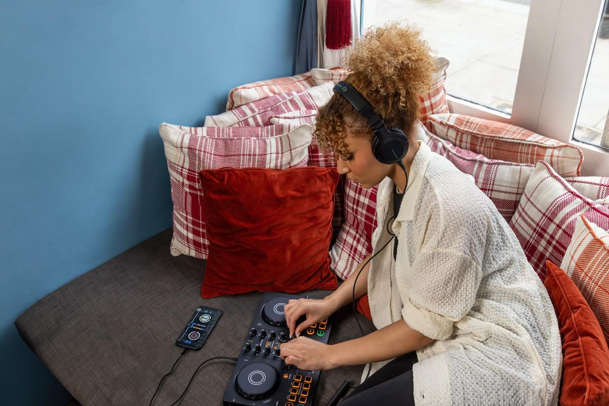 Eine Person, die DJ-Equipment mit Telefon, Kopfhörern und Mischpult benutzt.