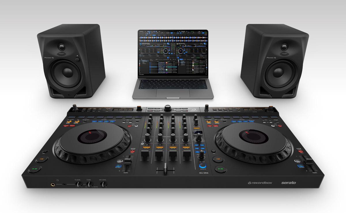DJ-Setup mit Laptop, Lautsprechern und Mischpult auf weißer Oberfläche.