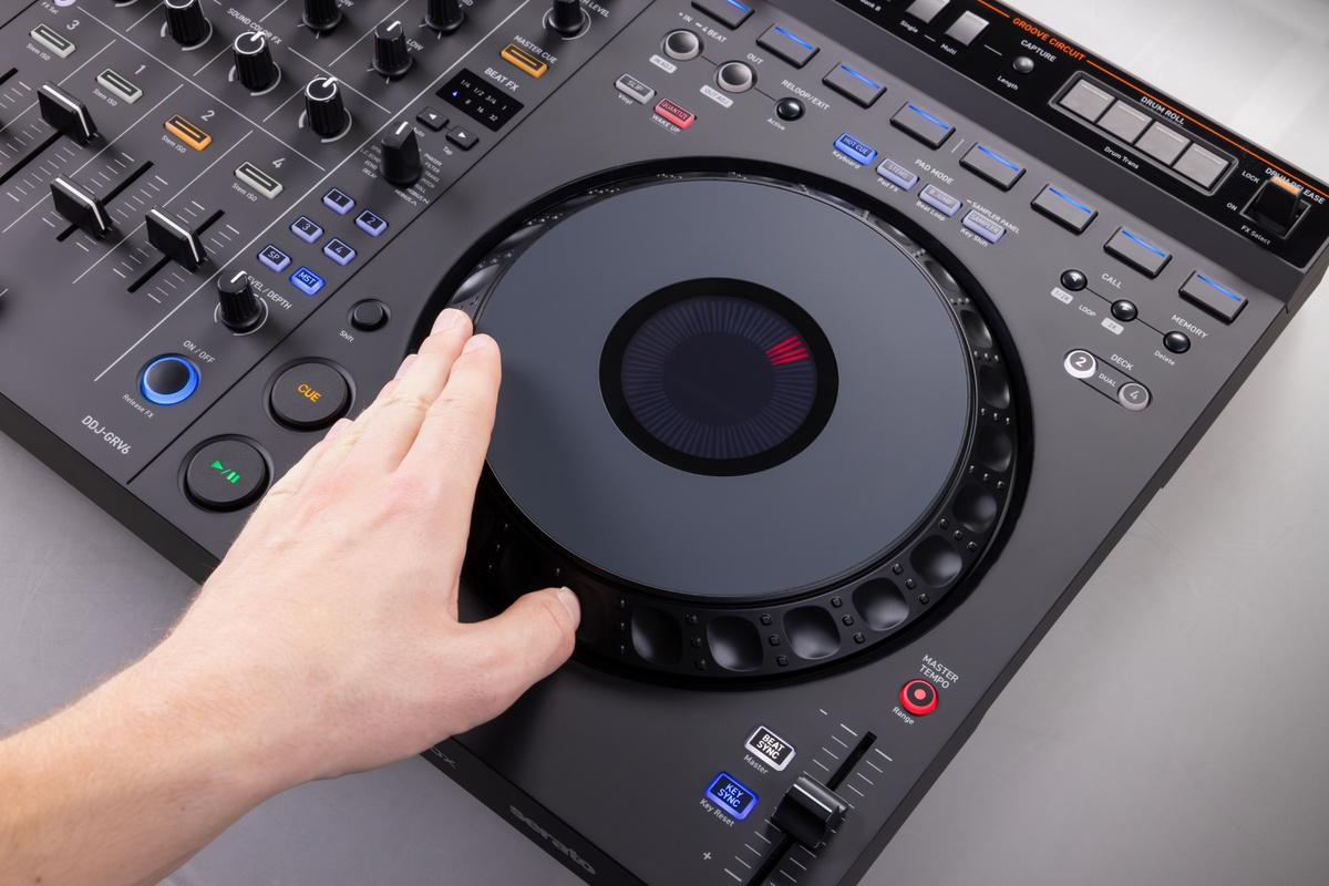 Eine Hand auf einem schwarzen DJ-Controller mit einem kreisförmigen Jogwheel und verschiedenen Tasten.