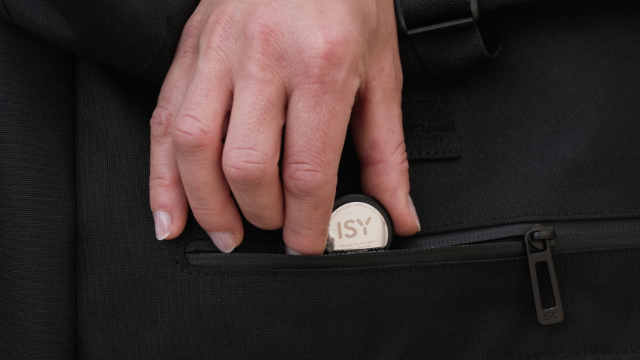 Hand, die einen kreisförmigen ISY-Gegenstand in eine schwarze Tasche legt.