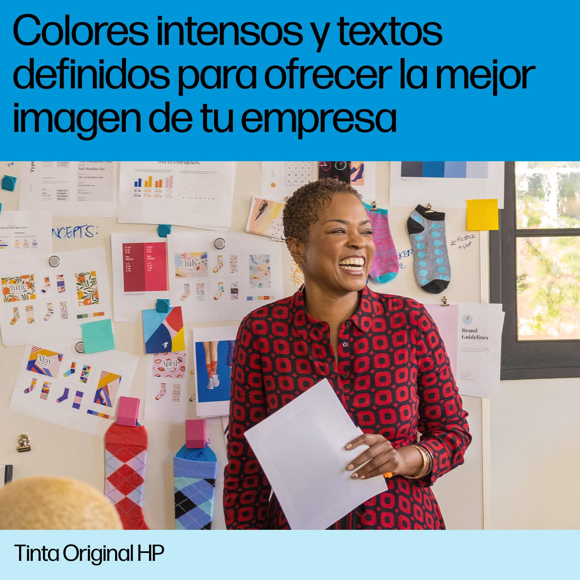 Una mujer sonriendo, sosteniendo un papel frente a una pared cubierta de objetos y texto coloridos.