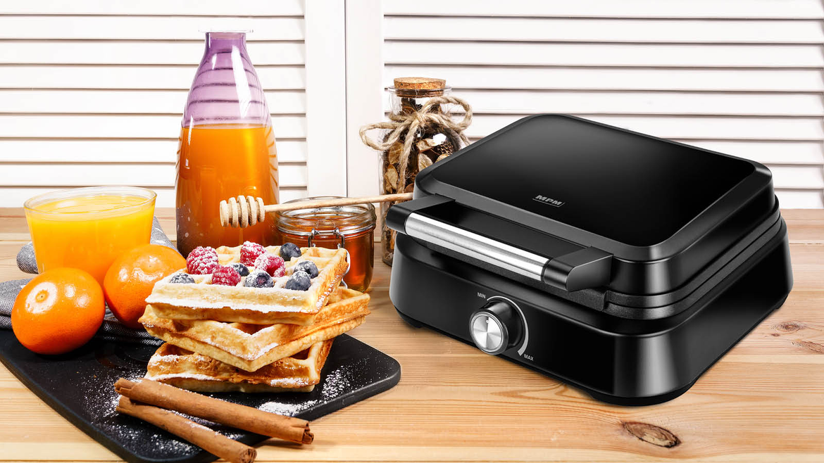 Czarny gofrownica z goframi, owocami i syropem. Scena rozgrywa się na drewnianym stole.