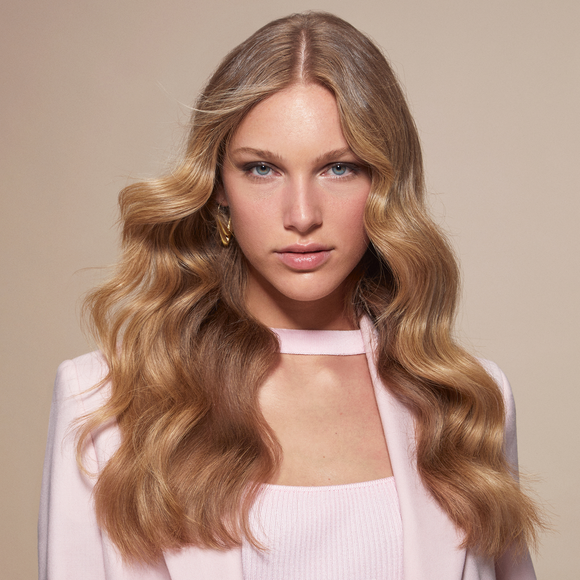 Egy szőke hajú nő, hullámos hajjal és rózsaszín öltönnyel.