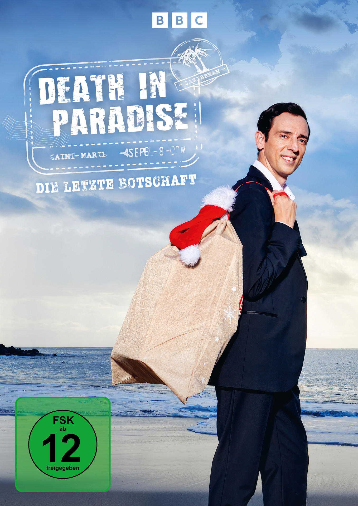 Death in Paradise DVD-Cover. Mann im Anzug trägt einen Weihnachtsmann-Beutel am Strand.