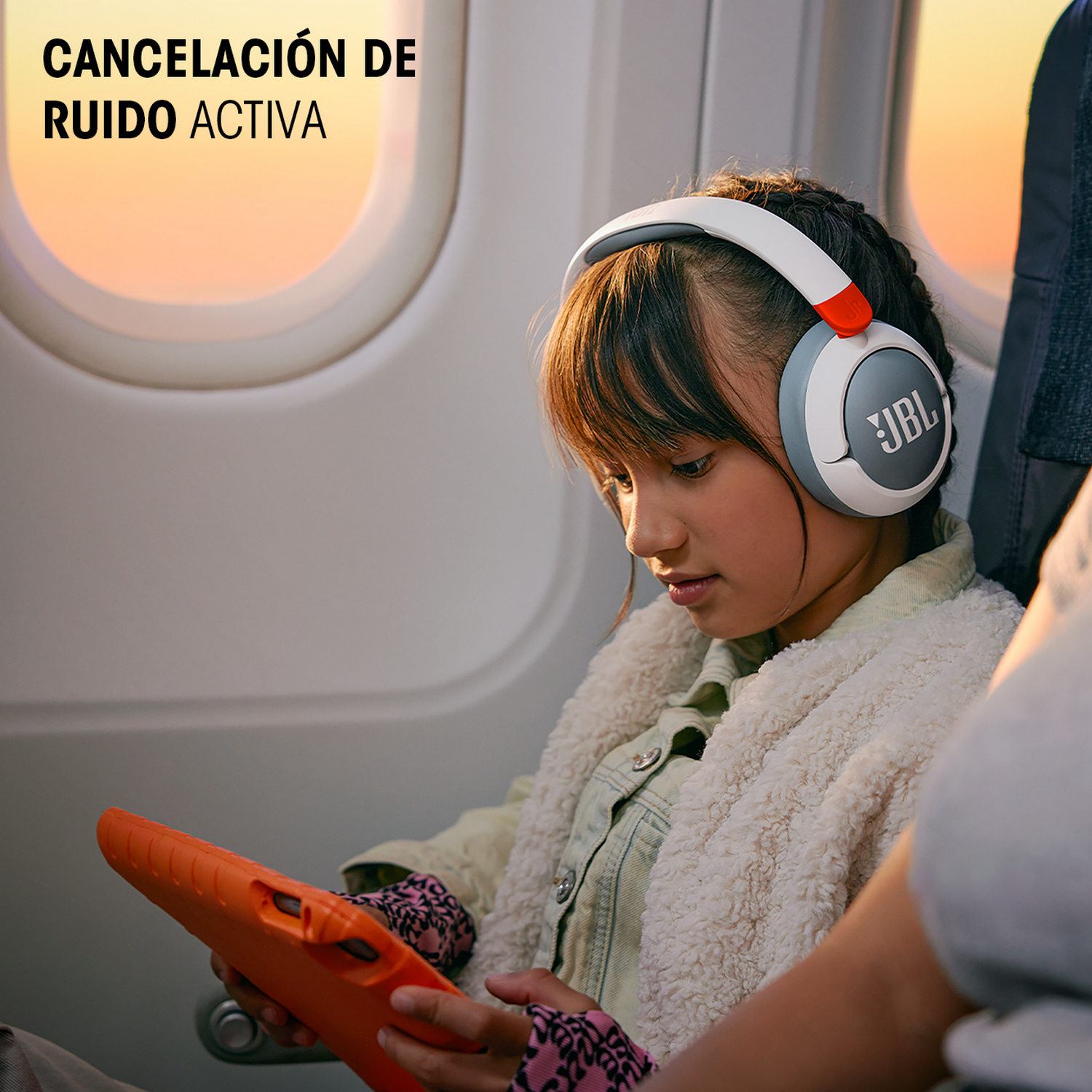 Niña con auriculares, mirando una tableta. Texto: Cancelación activa de ruido. Auriculares naranja y blancos.